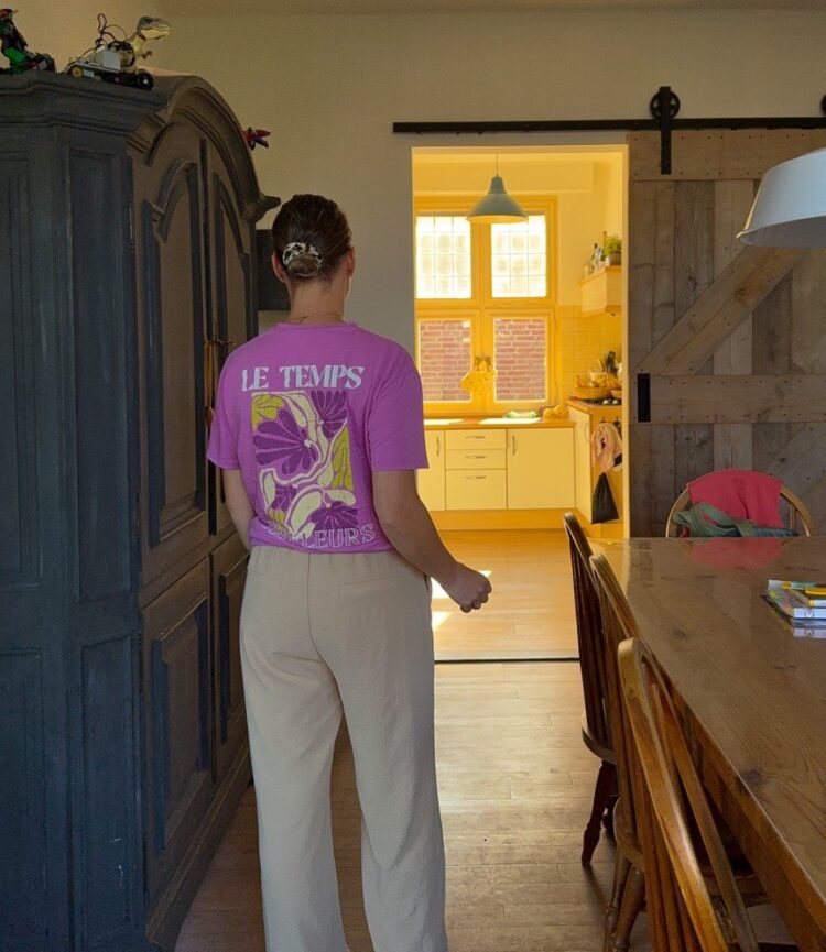 Nicky van Pol staand in de woonkamer van achteren met een roze shirt en beige broek.