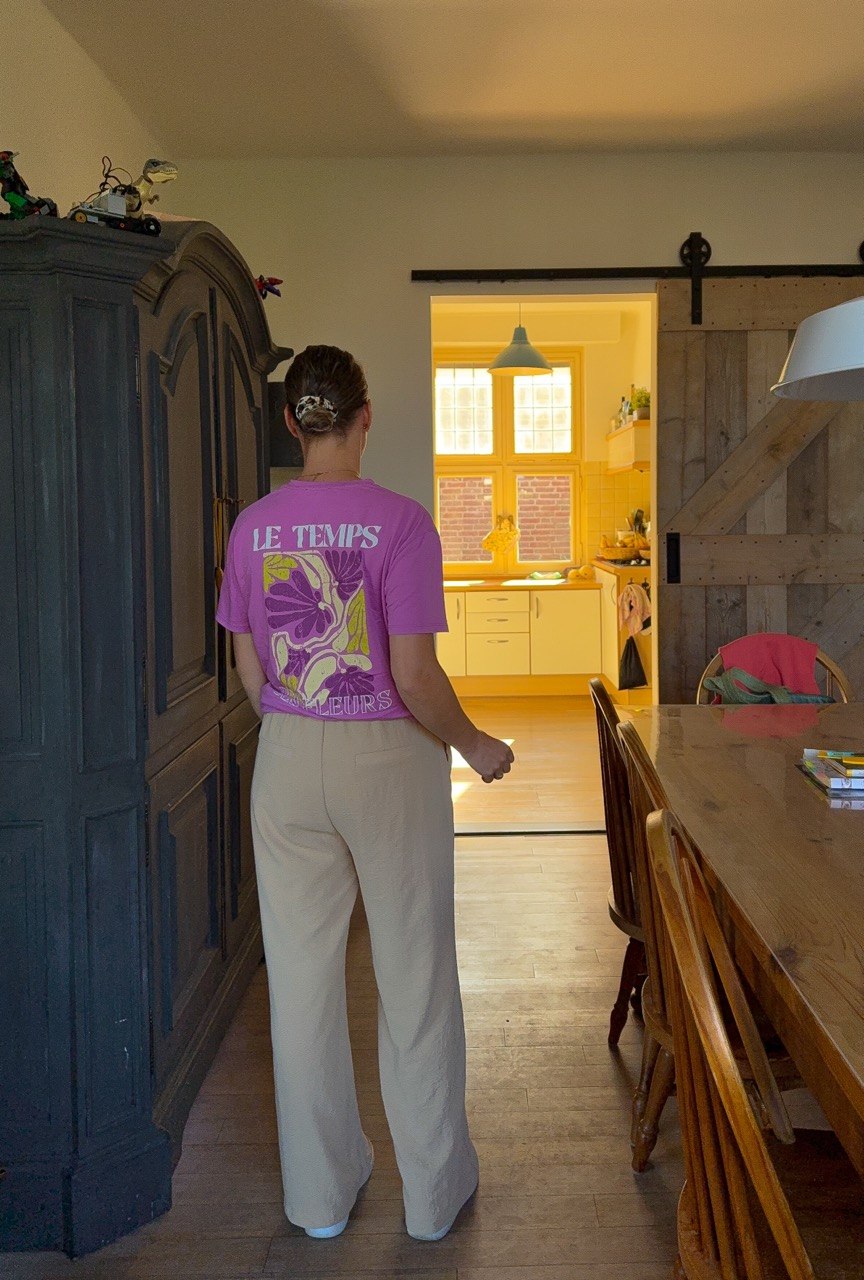 Nicky van Pol staand in de woonkamer van achteren met een roze shirt en beige broek.
