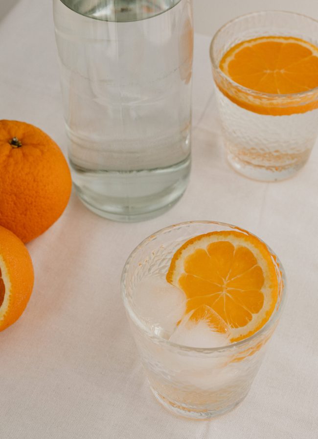 Frisse sappige sinaasappel in een glas water en een fles water